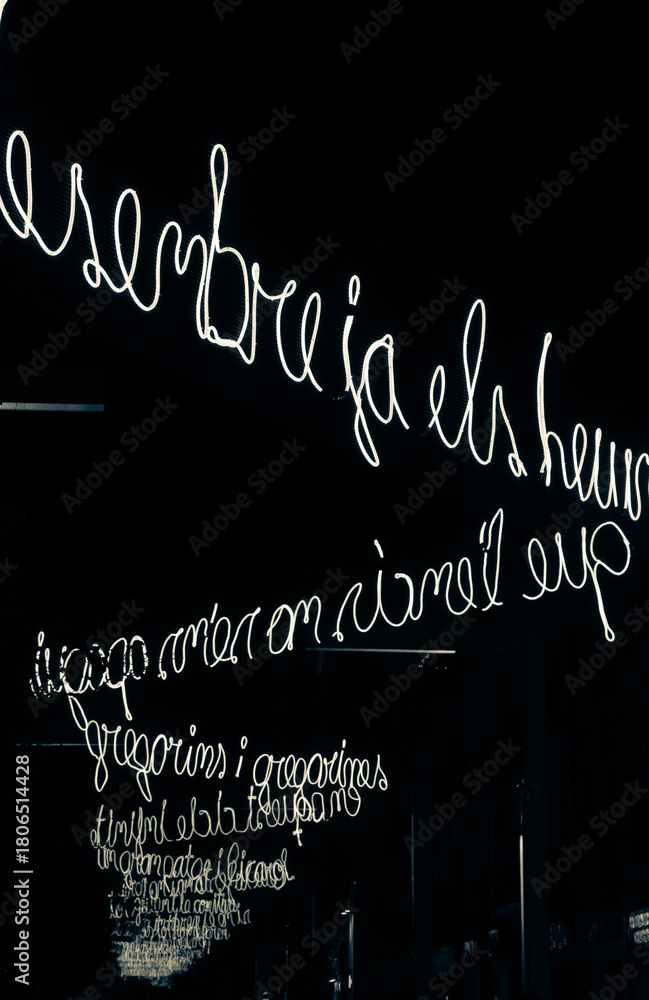 Fototapeta premium Illuminated calligraphic text on a dark street with Christmas lights at night.