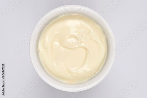 A creamy white chocolate pudding in a round plastic container is captured from a top-down view on a white background