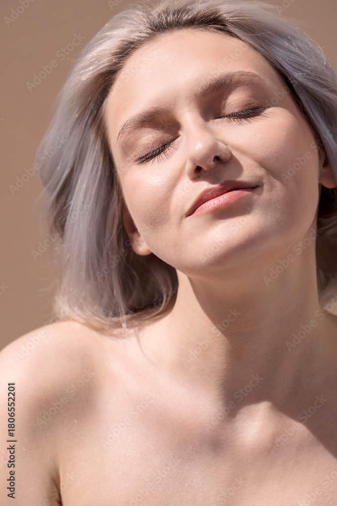 Naklejka premium Young woman with light hair, eyes closed, enjoying sunlight on her face, showcasing natural beauty and tranquility in a serene atmosphere, emphasizing relaxation and self-care