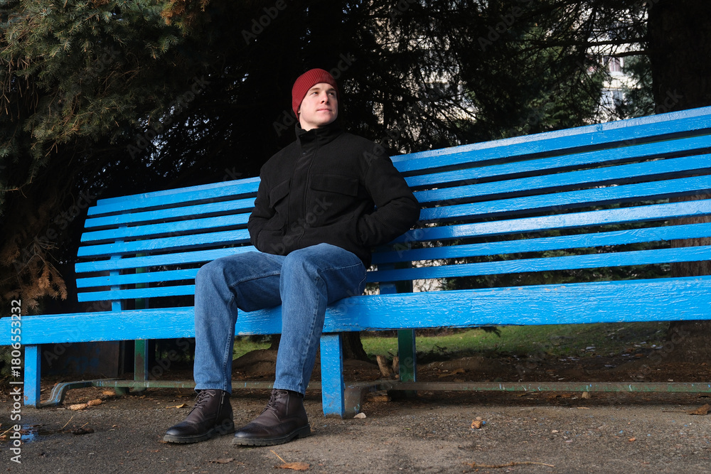 Fototapeta premium Man sitting on blue park bench looking pensive