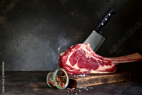 Raw organic tomahawk beef steak with meat cleaver on a wooden cutting board.