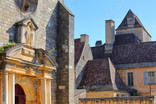 The entrance to the Catholic church Notre Dame de l'Assomption (Our Lady of the Assumption) in the fortified village Domme, Dordogne, France, with historical medieval houses and sloping slate roofs