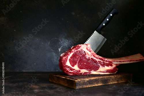 Raw organic tomahawk beef steak with meat cleaver on a wooden cutting board.