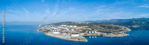 Aerial view of a sprawling industrial complex with numerous storage tanks and a towering chimney, juxtaposed against the deep blue sea, Rijeka, Primorje-Gorski Kotar County, Croatia.