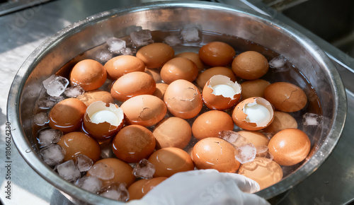 A stainless steel bowl of bolied eggs in a cold water some of them are crack