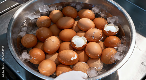 A stainless steel bowl of bolied eggs in a cold water some of them are crack