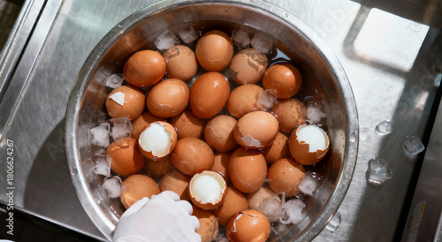 A stainless steel bowl of bolied eggs in a cold water some of them are crack