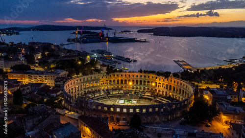 Aerial view of the illuminated Pula Arena standing proud against the fading twilight over the Adriatic Sea, a beacon of history and architectural wonder, Pula, Istria County, Croatia.