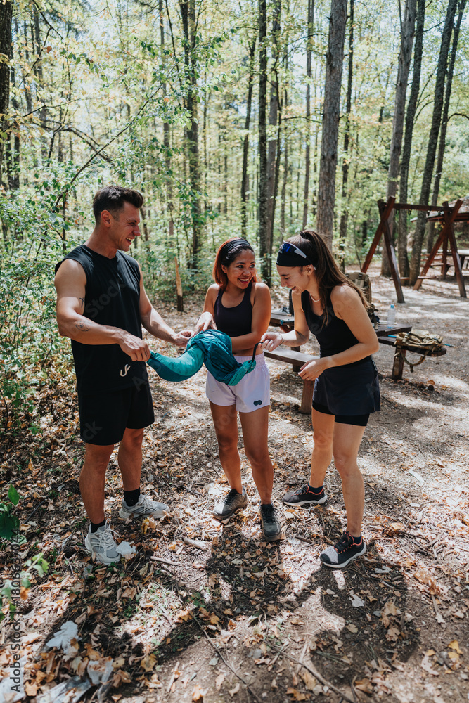 Fototapeta premium Three adults in a sunlit forest hold a toddler's hands, guiding a playful walk during a hike. A joyful, energetic moment of friendship and family bonding in nature.