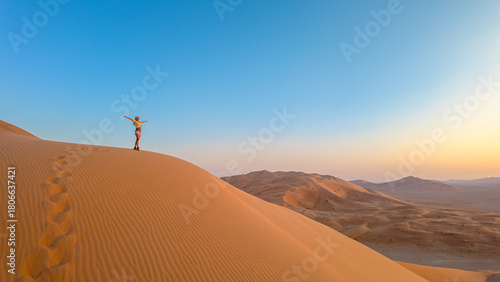 Aerial view of an adventure woman conquering Empty Quarter dunes in Oman, a solitary ascent against golden sands. Girl climbing the Rub' al-Khali desert dunes at sunset.