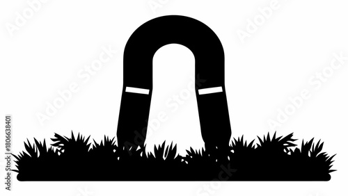 A black silhouette of a horseshoe magnet with white accents sitting in a field of grass in silhouette
