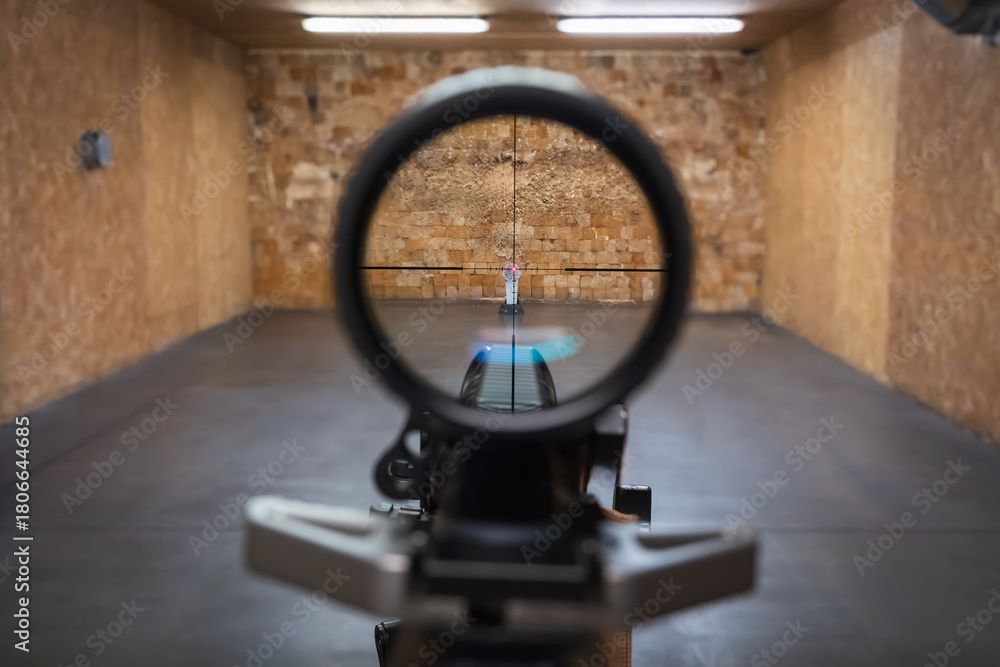 Naklejka premium First person view looking through a rifle optical sight aiming at a metal popper target at an indoor shooting range