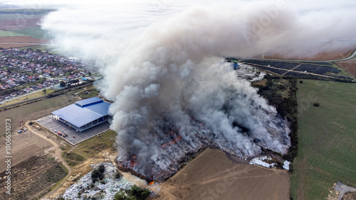 Aerial view of a thick plume of smoke billowing from a burning landfill near a building, casting a stark contrast against the muted landscape, Osijek, Osijek-Baranja County, Croatia.