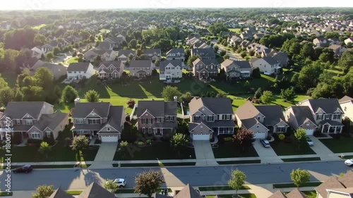 An aerial shot of a suburban neighborhood, showcasing rows of houses with manicured lawns and trees, bathed in sunlight