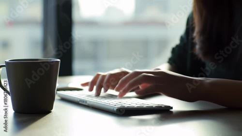 Hands typing on a keyboard, with a coffee mug in the foreground. Soft light illuminates the scene, suggesting a window and early morning