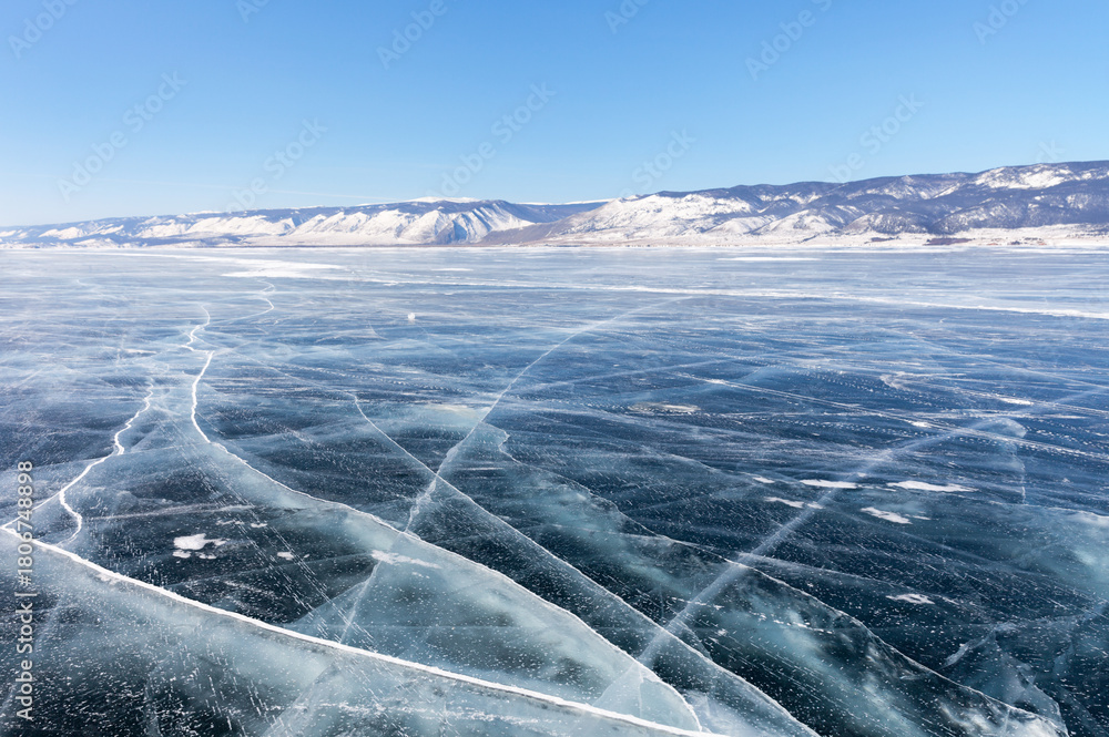 Fototapeta premium Baikal Lake on sunny February day. View of ice-covered Small Sea and ice road from Olkhon Island. Winter ice travel and adventure. Natural background. Scenic winter icy landscape