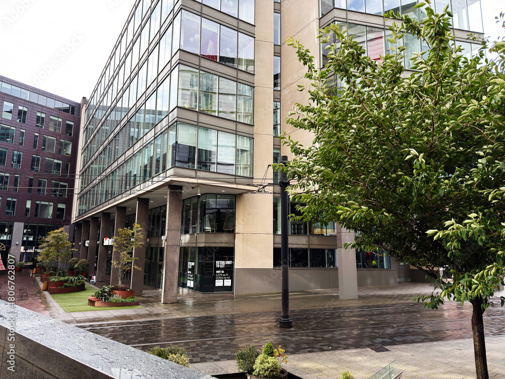 Fototapeta premium Modern office building street scene in Manchester, UK with glass facade and urban trees