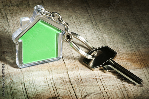 Metallic key with house-shaped keychain on wood, symbolizing homeownership and property access.