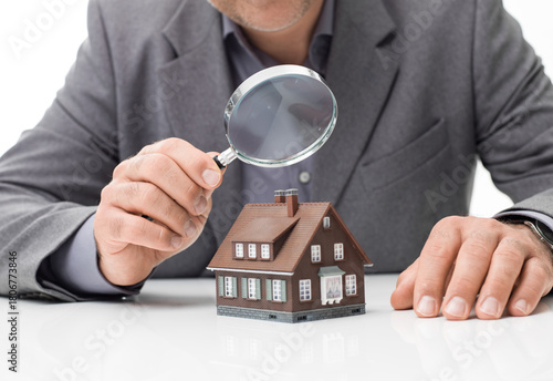 Businessperson inspecting house model with magnifying glass, symbolizing property evaluation and appraisal.
