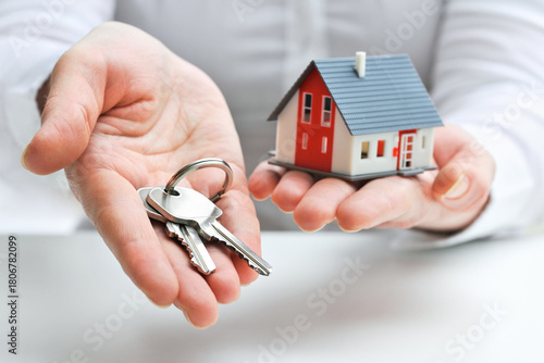 Person holding house model with key, symbolizing homeownership and real estate acquisition.