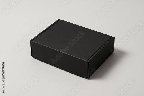 Fotografie A simple closed black rectangular cardboard box resting on a plain light gray surface
