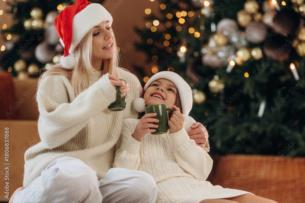 Naklejka premium Green cups of tea are in hands. Mother and daughter are celebrating New Year at home in domestic room