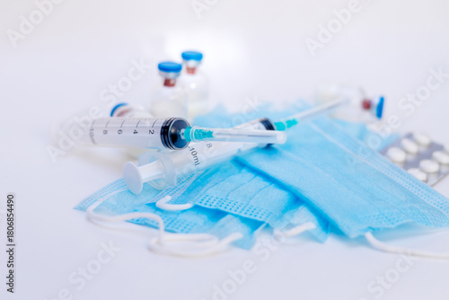 A still life of medical syringes and medication vials. Disposable syringes, medical masks, and fever pills. Supplies for injections and virus protection. 