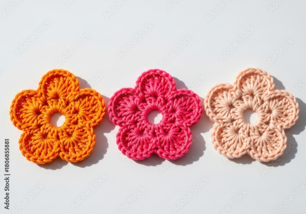 Obraz premium Three colorful crocheted flowers in orange pink and beige isolated on white background