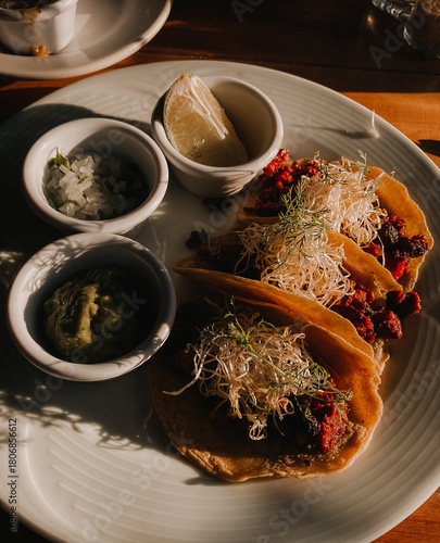 Close-up of freshly prepared tacos served with guacamole, onions and lime. Traditional Mexican cuisine, vibrant colors, delicious street-food presentation and warm natural light.