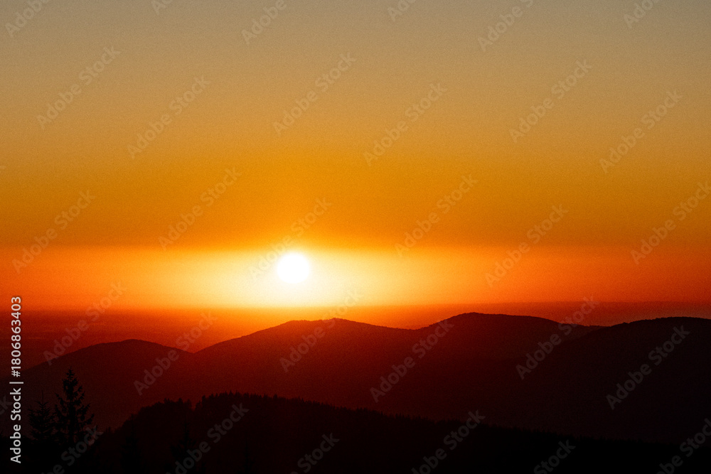 Fototapeta premium Soft sunrise over layered mountain ranges and a warm orange horizon. Hazy, calm, minimal, this soothing landscape captures quiet morning light, perfect for travel, wellness content, posters. Ads.