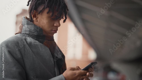 Young african man using smartphone on city street, male user of mobile phone. Portrait of black guy chatting in mobile app, scrolling news tape online, internet addicted people, entertainment in web