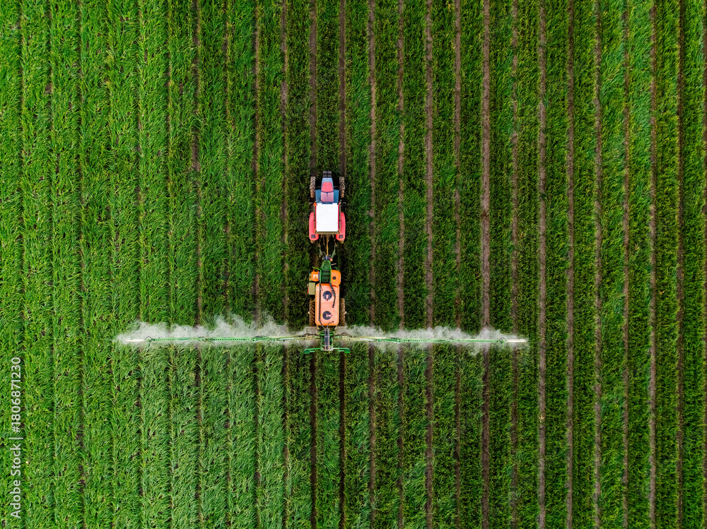 Obraz premium Tractor spraying pesticide on green agricultural crop field