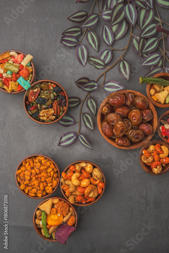 A variety of nuts and dried fruits are displayed in bowls on a grey background.