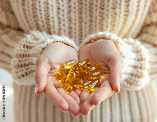 Close-up of hands holding golden omega-3 softgel capsules, symbolizing nutrition, wellness, and daily health supplements. Warm natural light and cozy sweater texture create a calm, healthy lifestyle m