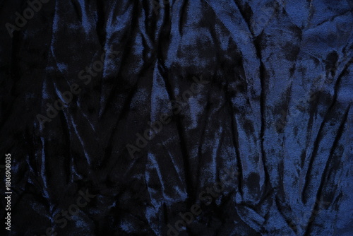 Dark blue velour fabric texture, close-up plush surface and natural folds. The detailed texture shows characteristic light reflections and smooth, velvety appearance typical for velour used in clothin