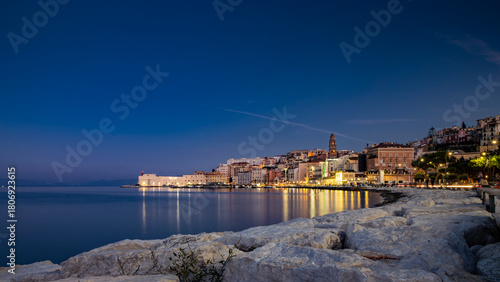 Fototapeta Naklejka Na Ścianę i Meble -  Gaeta, Latina, Lazio, Italy. A splendid night view of the city. The old town with its houses overlooking the sea. The waterfront and the lights of the harbor reflecting on the water.