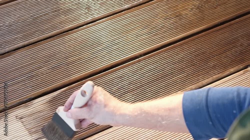 Brown oil for protection of wood by staining. Painting a larch for protecting and pests. Woodworker applying finish to terrace deck board. Repairman varnishing with brush wooden plank floor surface.