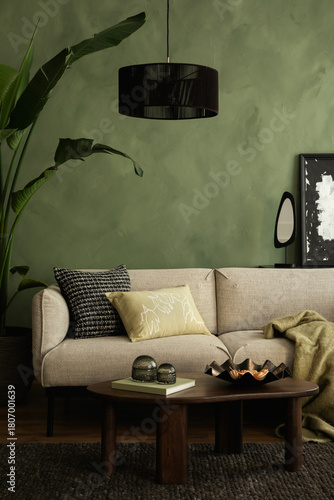 Modern living room with a beige sofa, green textured wall, black pendant lamp, and wooden coffee table with stylish decor.