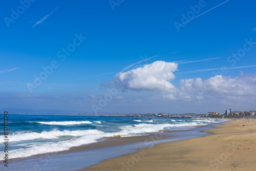 Redondo Beach coastline with waves, sand, and residential houses under a blue sky.