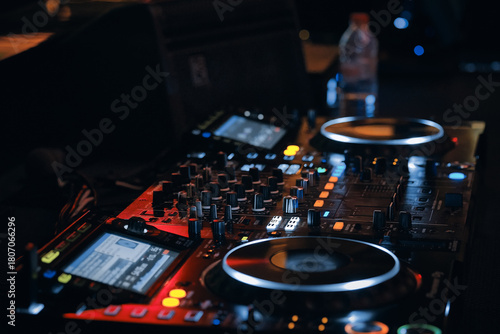 Professional DJ mixer setup with illuminated controls, dual turntables and glowing buttons in dark nightclub environment. Nightlife, music, creativity