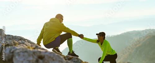 Two climbers assist each other while scaling a rocky mountain at sunrise. The golden light highlights their effort and teamwork on the challenging path