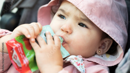 Toddler eating fruit puree from a pouch outdoors
