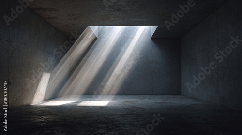 Light streams through an opening in the ceiling of a concrete room, creating a dramatic effect. The light illuminates the otherwise dark space, highlighting the texture of the walls and floor