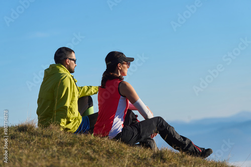 Two hikers enjoy a peaceful moment on a hillside overlooking a stunning landscape during a sunny day