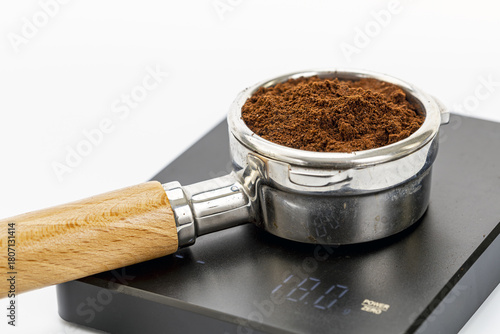 Close-up of metal portafilter filled with espresso coffee grounds on digital scale displaying weight measurement