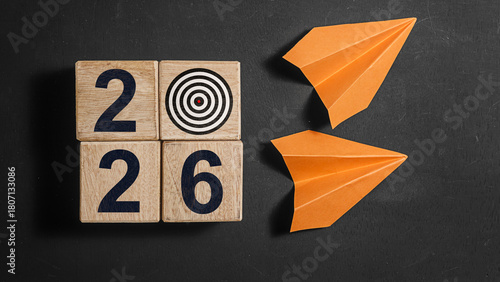 2026 Happy New Year. Wooden cube block 2026 greeting card on Blackboard with 2 orange paper planes. Concept 2026 New Year background. Business, resolutions, goals, inspiration, success, ideas . High