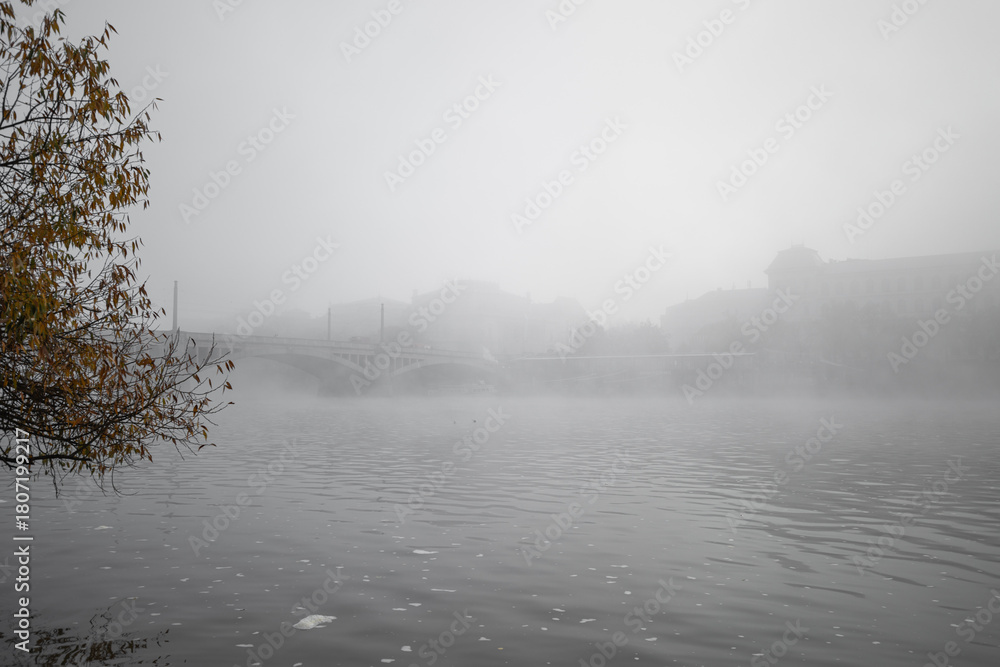 Fototapeta premium Vltava river flowing through thick fog covering Manes bridge and Rudolfinum, creating a mysterious atmosphere in prague
