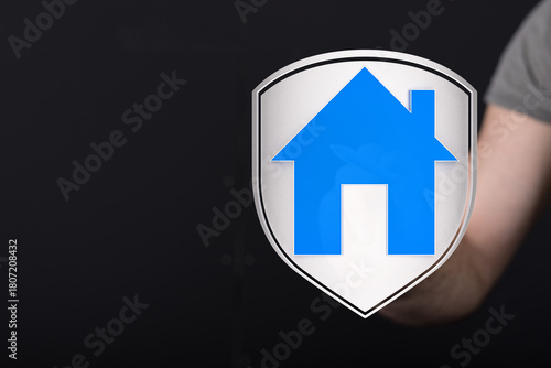 Free Download A hand holding a blue house symbol shield against a dark background representing home protection, security, and real estate. - GFXLoad