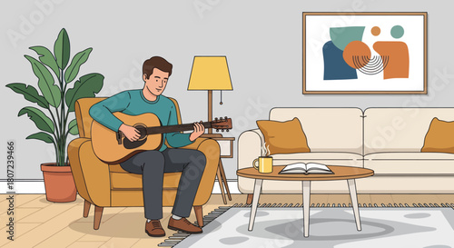 A man plays an acoustic guitar seated in a cozy armchair in a living room, with a couch, art, and plant
