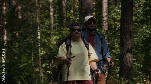 Wallpaper Mural Man and young woman with down syndrome, wearing sunglasses, backpacks, and using hiking poles, hiking through sun-dappled forest Torontodigital.ca